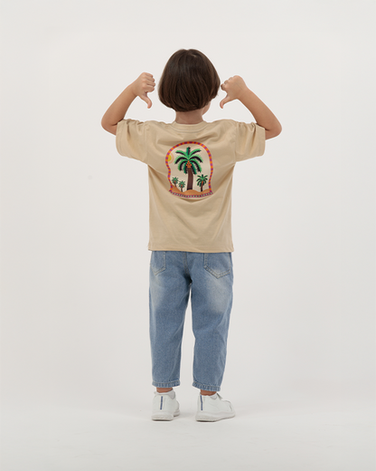 Kid boy in beige The Palm T-Shirt featuring colorful palm trees.