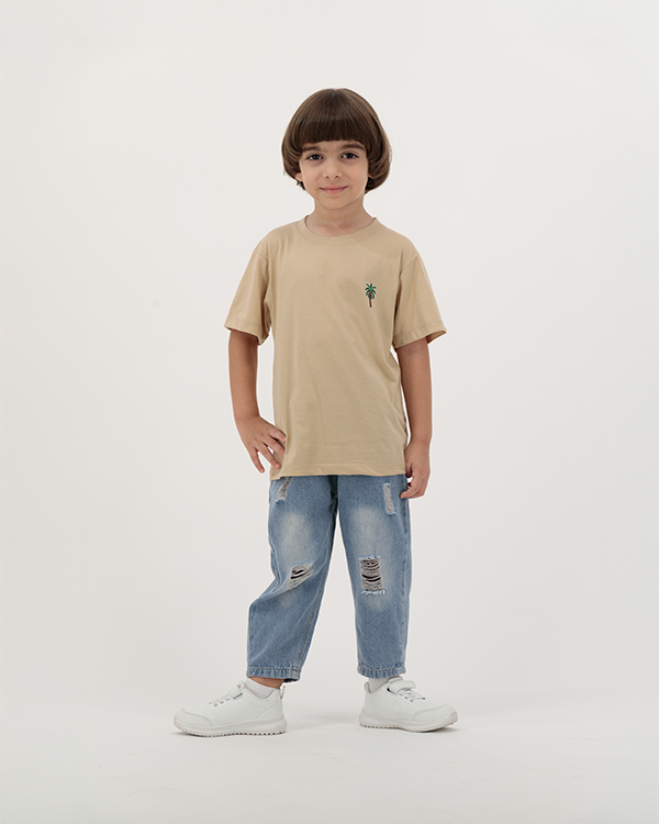 Boy in beige The Palm T-Shirt featuring palm trees and sun print.