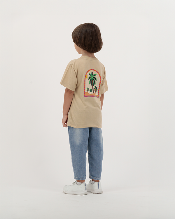 Young boy dressed in The Palm Kids beige T-Shirt with tropical print on back.
