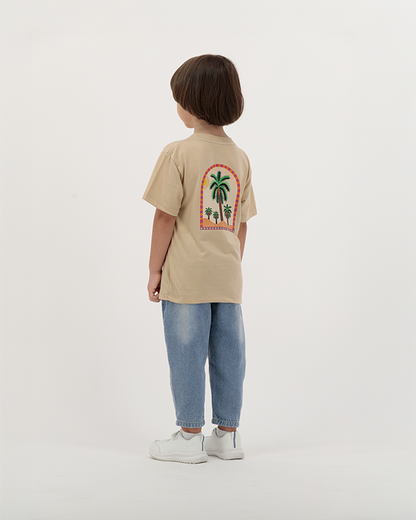 Young boy dressed in The Palm Kids beige T-Shirt with tropical print on back.