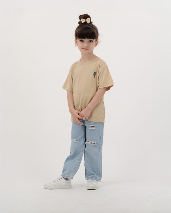 Girl wearing beige The Palm Kids Leaf Print T-Shirt with palm design on back.