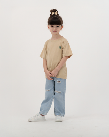 Girl wearing beige The Palm Kids Leaf Print T-Shirt with palm design on back.