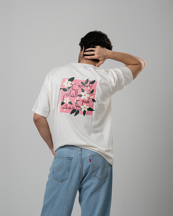 Man dressed in Jasmine White T-Shirt with pink floral artwork on back.